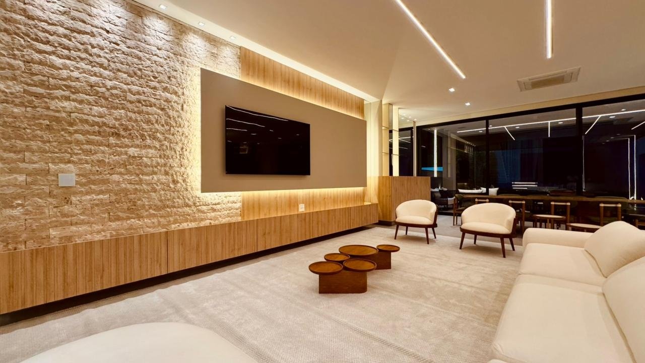 Parede do living com pedra, painel de TV e luz indireta acima de uma base longa de marcenaria.