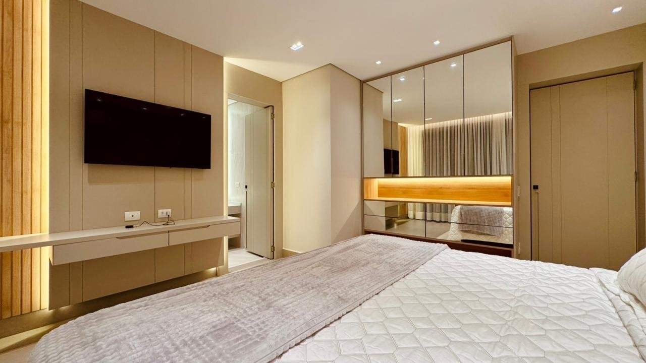 Suíte com cama clara, painel de TV e armários espelhados com faixa de marcenaria iluminada.